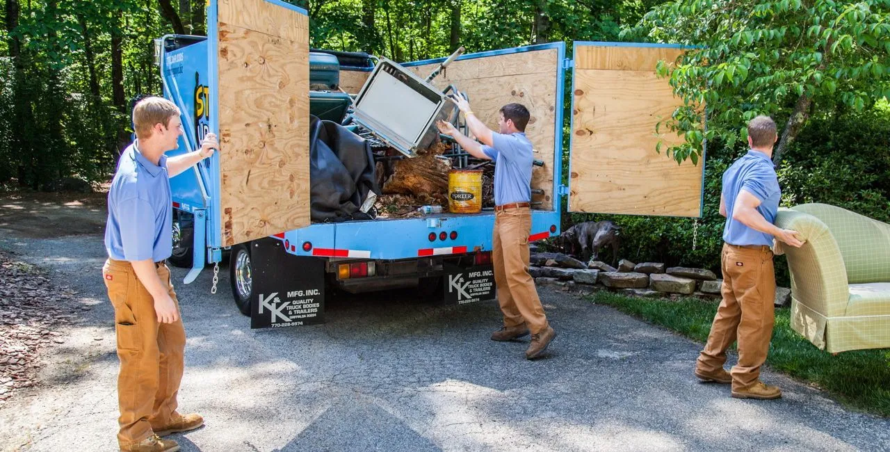 Junkisremoved team loading old furniture, appliances, and household junk into a removal truck during a residential cleanout.
