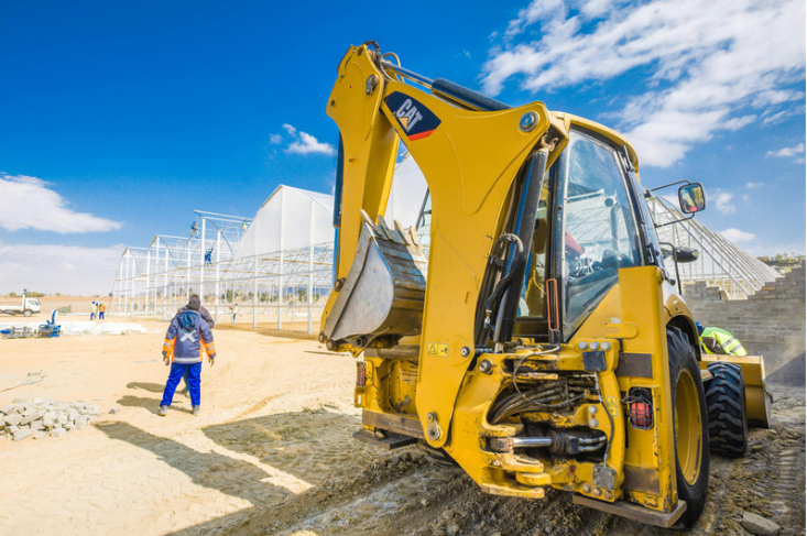 Backhoe loader performing excavation work under clear blue skies.